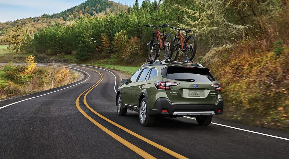 Rear of a green 2024 Subaru Outback driving down a winding road.