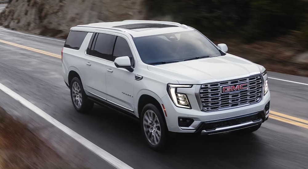 A white 2026 GMC Yukon Denali driving on a highway.