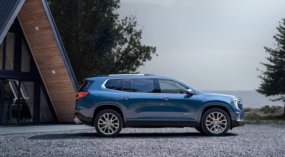 A blue 2026 GMC Acadia parked near a cabin.