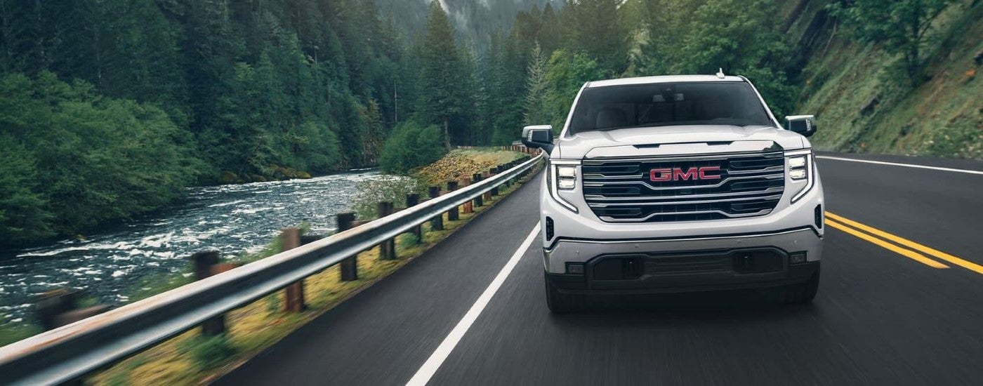 White 2024 GMC Sierra 1500 SLE driving along a river