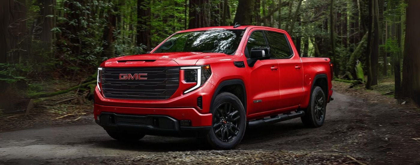 Red 2026 GMC Sierra 1500 parked off-road in a forest.