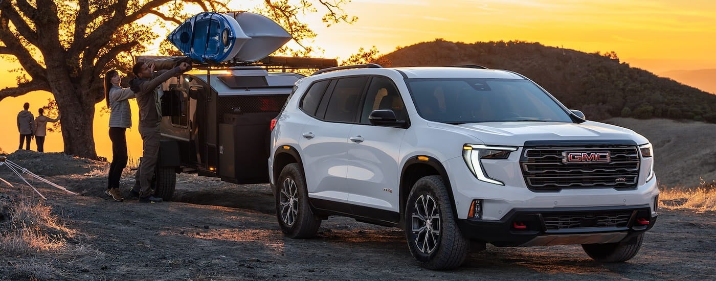 White 2026 GMC Acadia towing a trailer off-road.