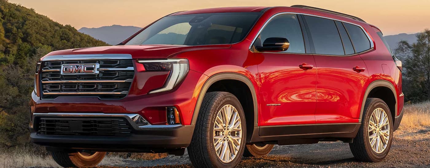 Side of a red 2026 GMC Acadia Denali driving off-road.