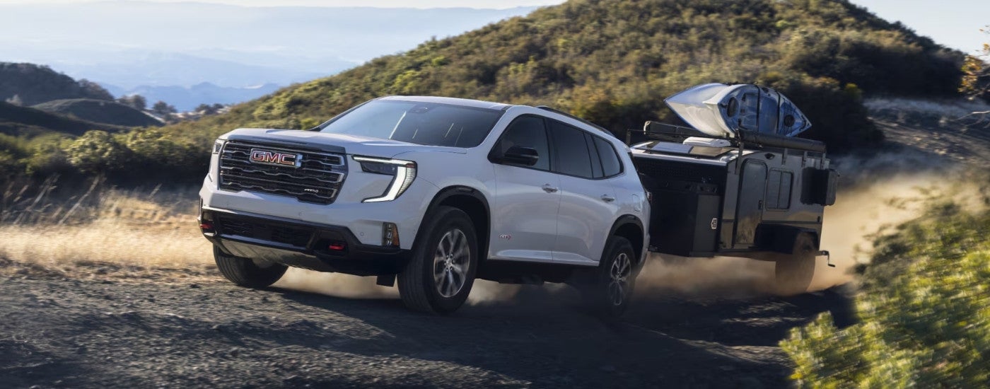 A white 2025 GMC Acadia AT4 is shown driving to a GMC dealer.