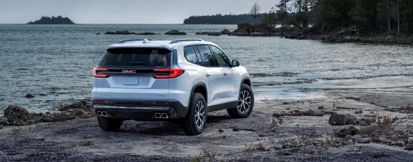 Rear of a white 2024 GMC Acadia AT4 parked by a lake.