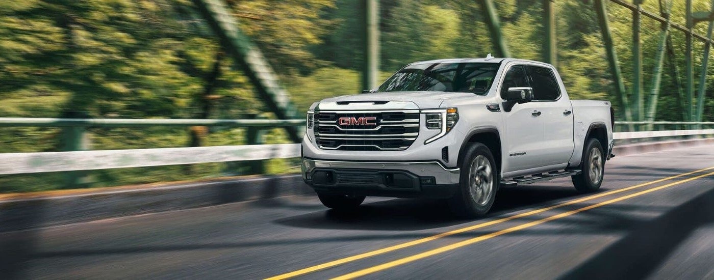 Side of a white 2024 GMC Sierra 1500 SLE driving down a bridge.