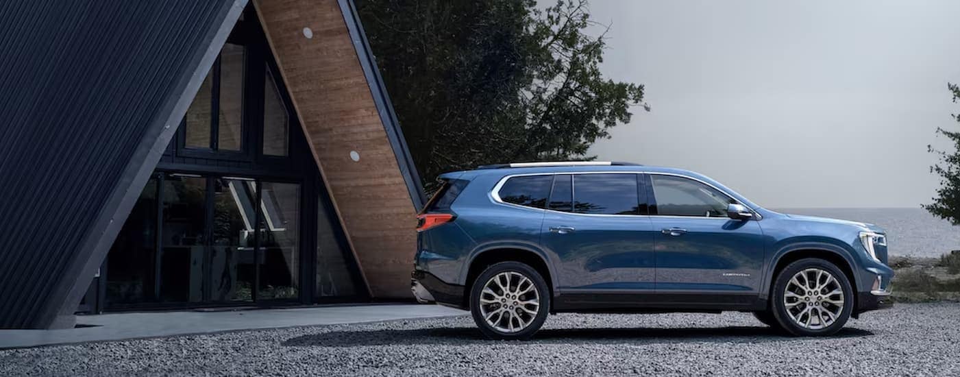 A blue 2025 GMC Acadia parked near an A-frame cabin.