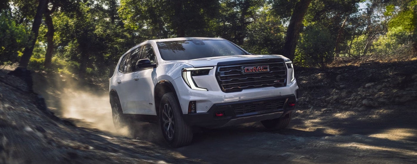 A white 2025 GMC Acadia AT4 is shown from the front at an angle.